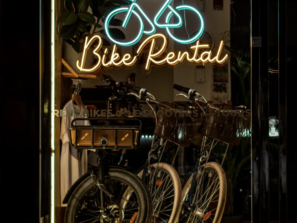 A neon shop sign glowing above a bicycle shop doorway at night