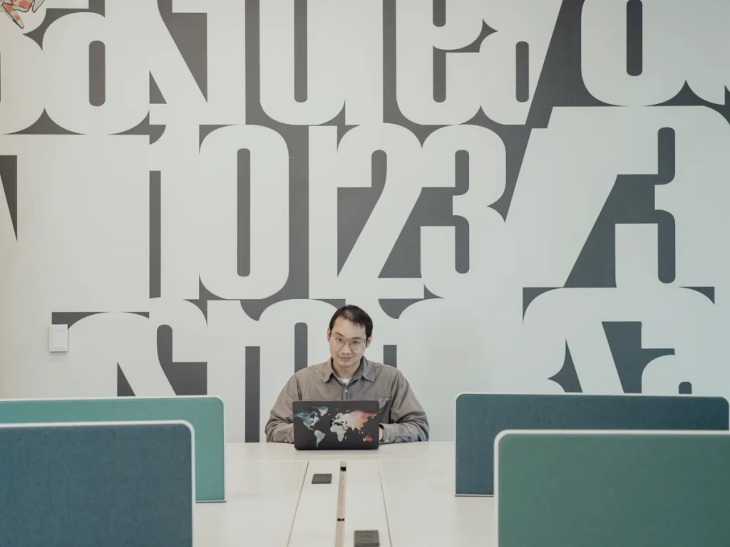 A full-height printed typography graphic on an office wall behind a desk